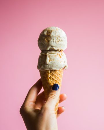 hand holding vanilla ice cream cone on pink background